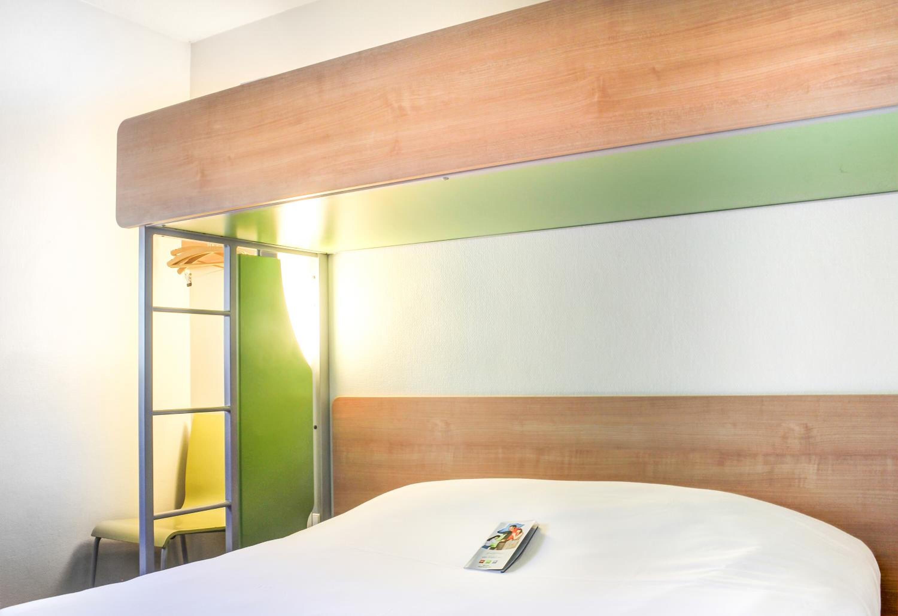 Une chambre d’hôtel avec un lit, une tête de lit en bois, un mur vert et une chaise.