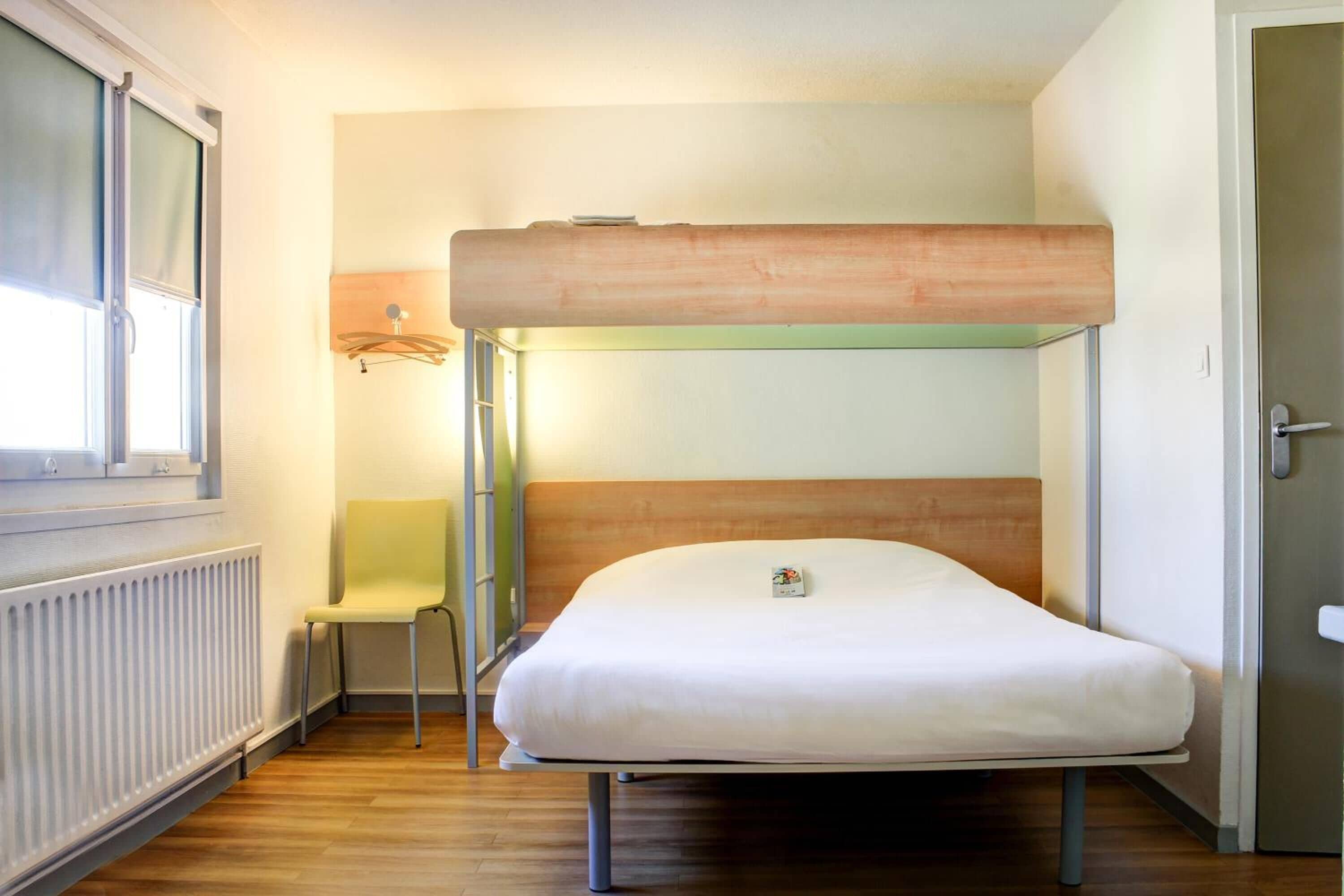 Un lit superposé avec un matelas et une chaise dans une pièce équipée d’un radiateur et d’une fenêtre.