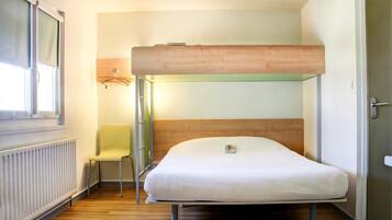 Un lit superposé avec un matelas et une chaise dans une pièce équipée d’un radiateur et d’une fenêtre.