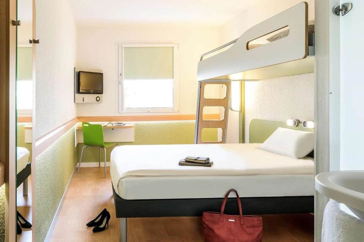 A hotel room with a bed, a desk, a chair, a TV, and a window.
