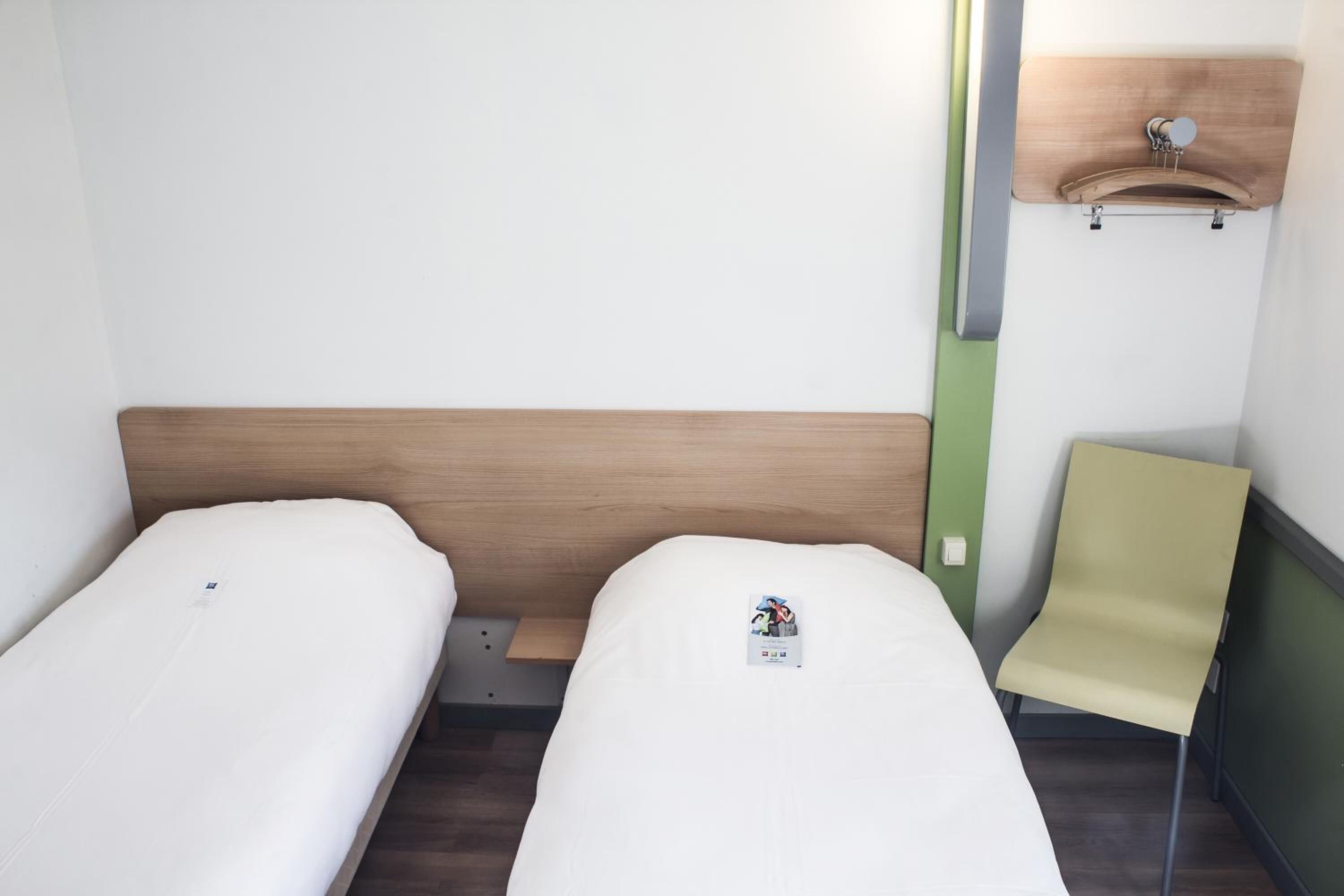 A small, clean room with two single beds, a wooden headboard, a green wall, and a yellow chair.