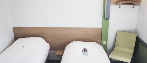 A small, clean room with two single beds, a wooden headboard, a green wall, and a yellow chair.