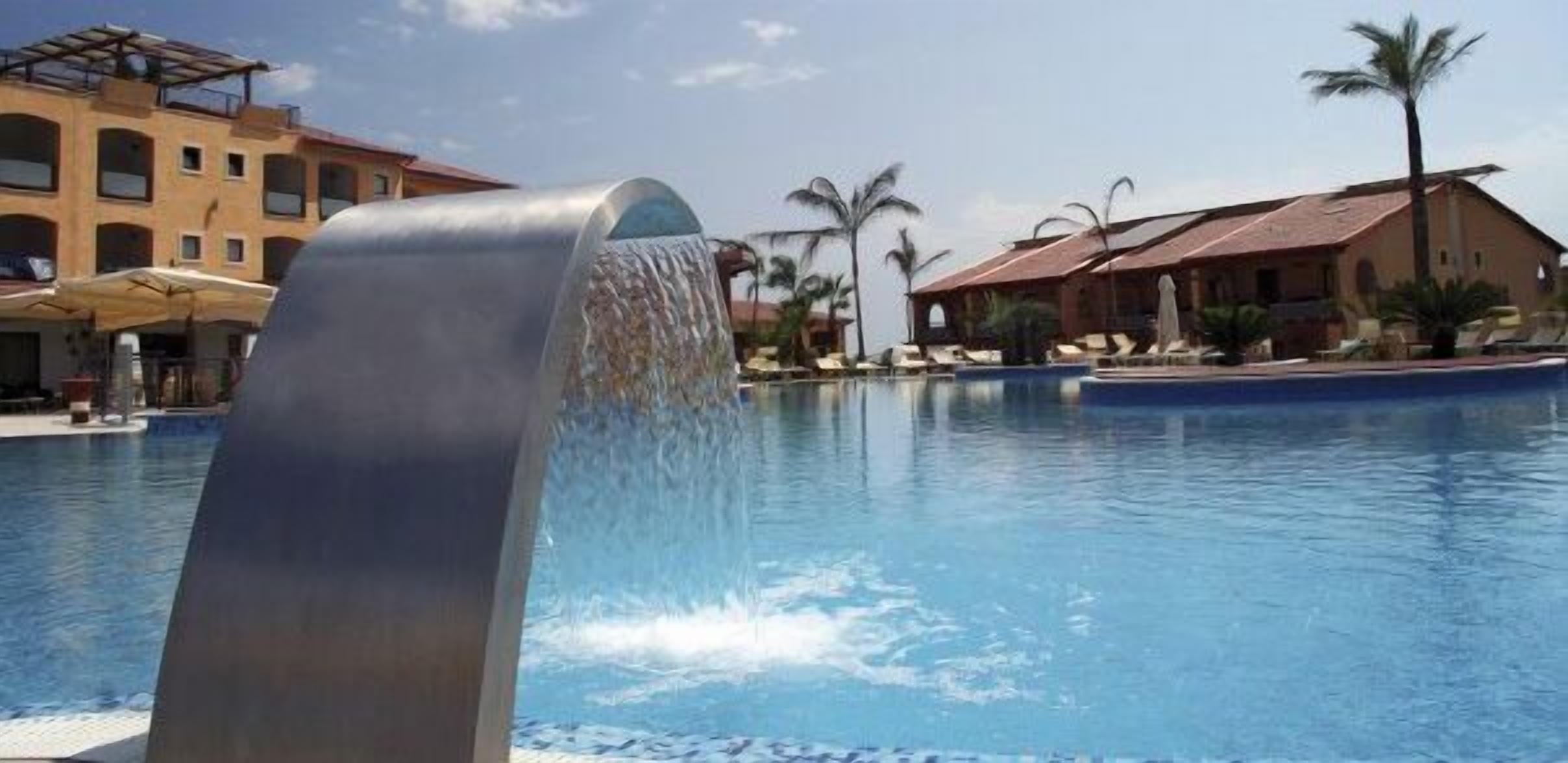 Una piscina con cascata, palme e un edificio con tetto rosso sullo sfondo.