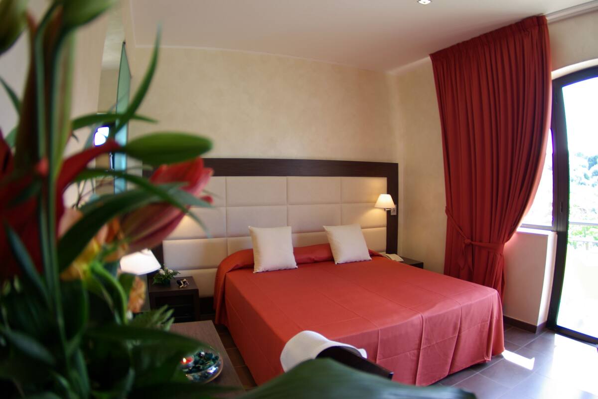 A hotel room with a large bed, a nightstand, a lamp, and a window with curtains.