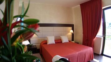 Una camera d'albergo con un letto grande, un comodino, una lampada e una finestra con tende.