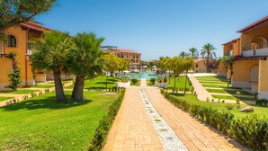 Un resort con piscina central, palmeras y un camino pavimentado.