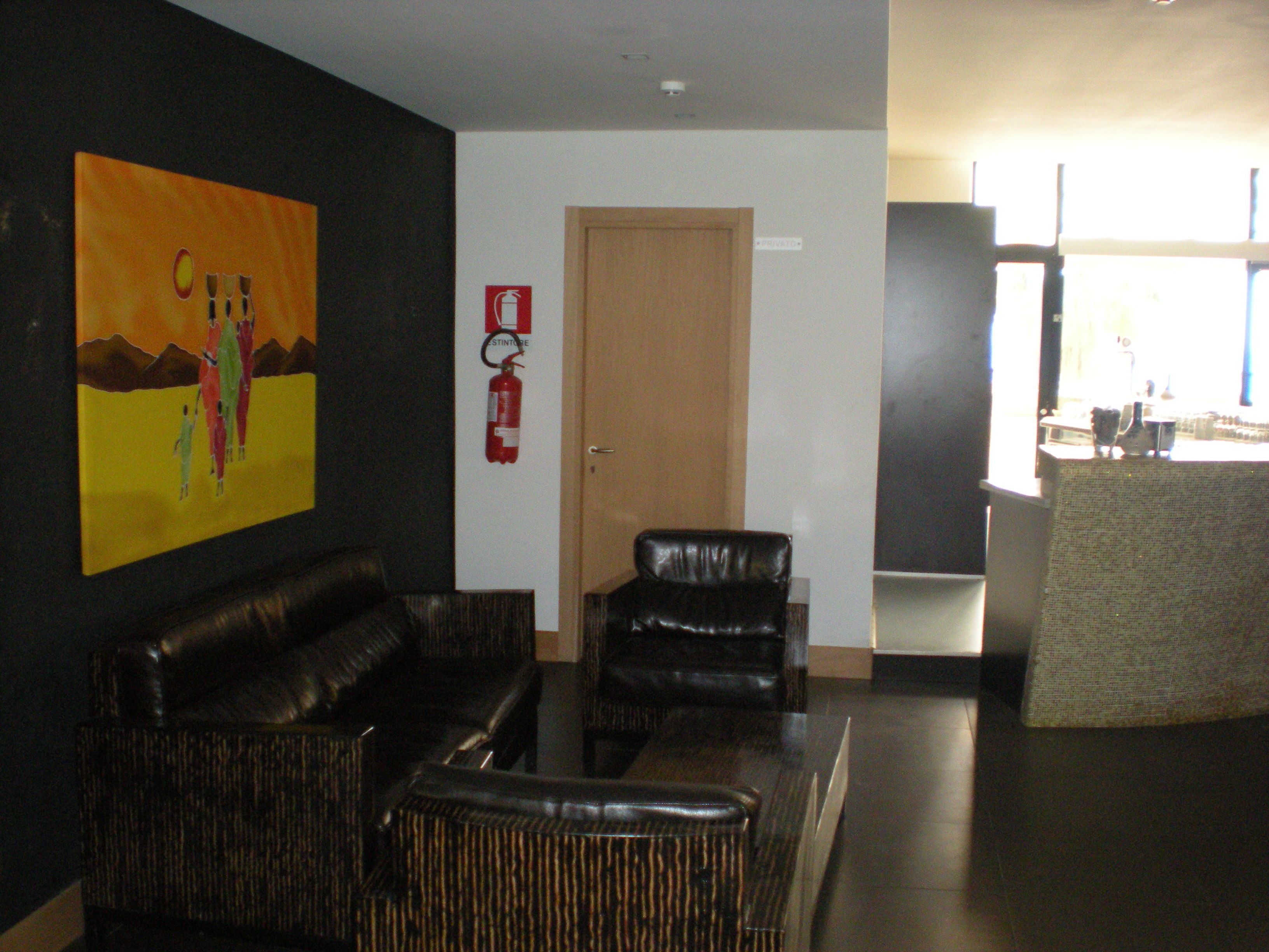 A lobby with a black leather sofa, a wooden door, and a fire extinguisher on the wall.