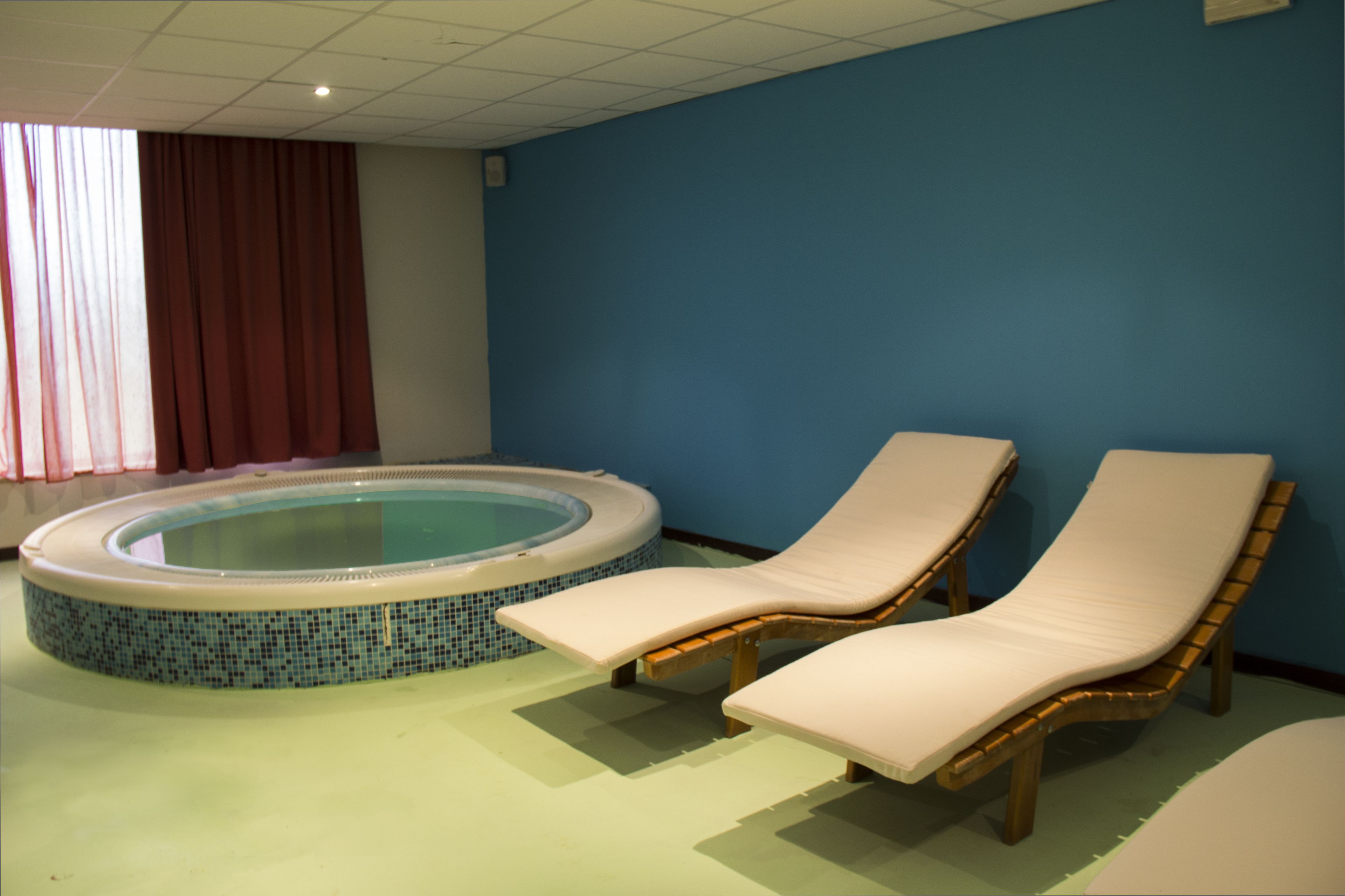 A spa room with a hot tub, two lounge chairs, and a blue wall.