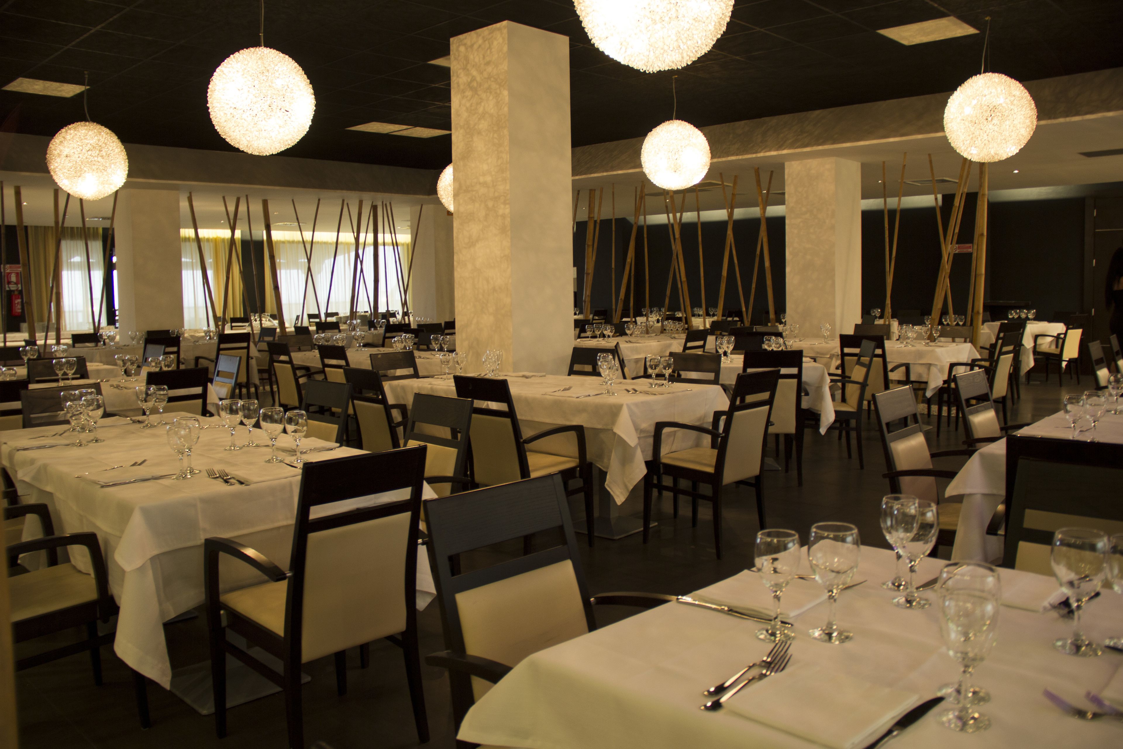 Een restaurant met meerdere eettafels, witte tafellinnen, stoelen en hangende, bolvormige kroonluchters.