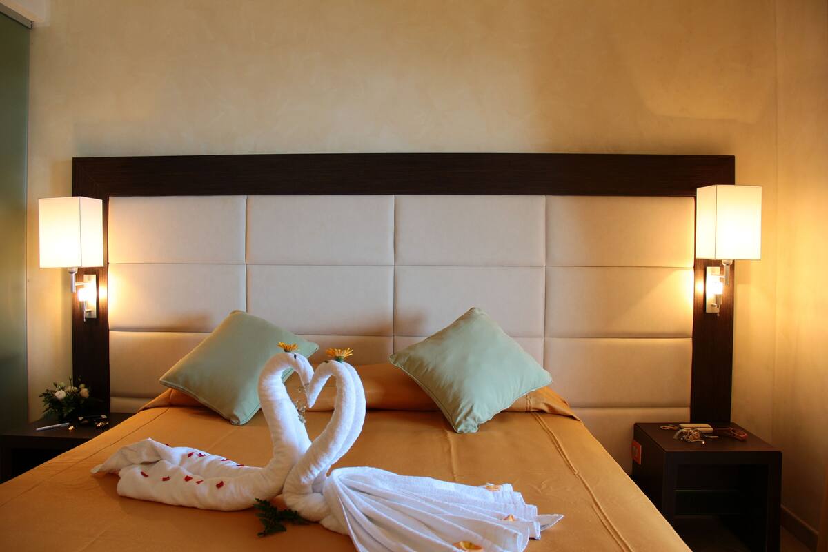 A hotel room with a large bed, two pillows, a nightstand, and two wall-mounted lamps.