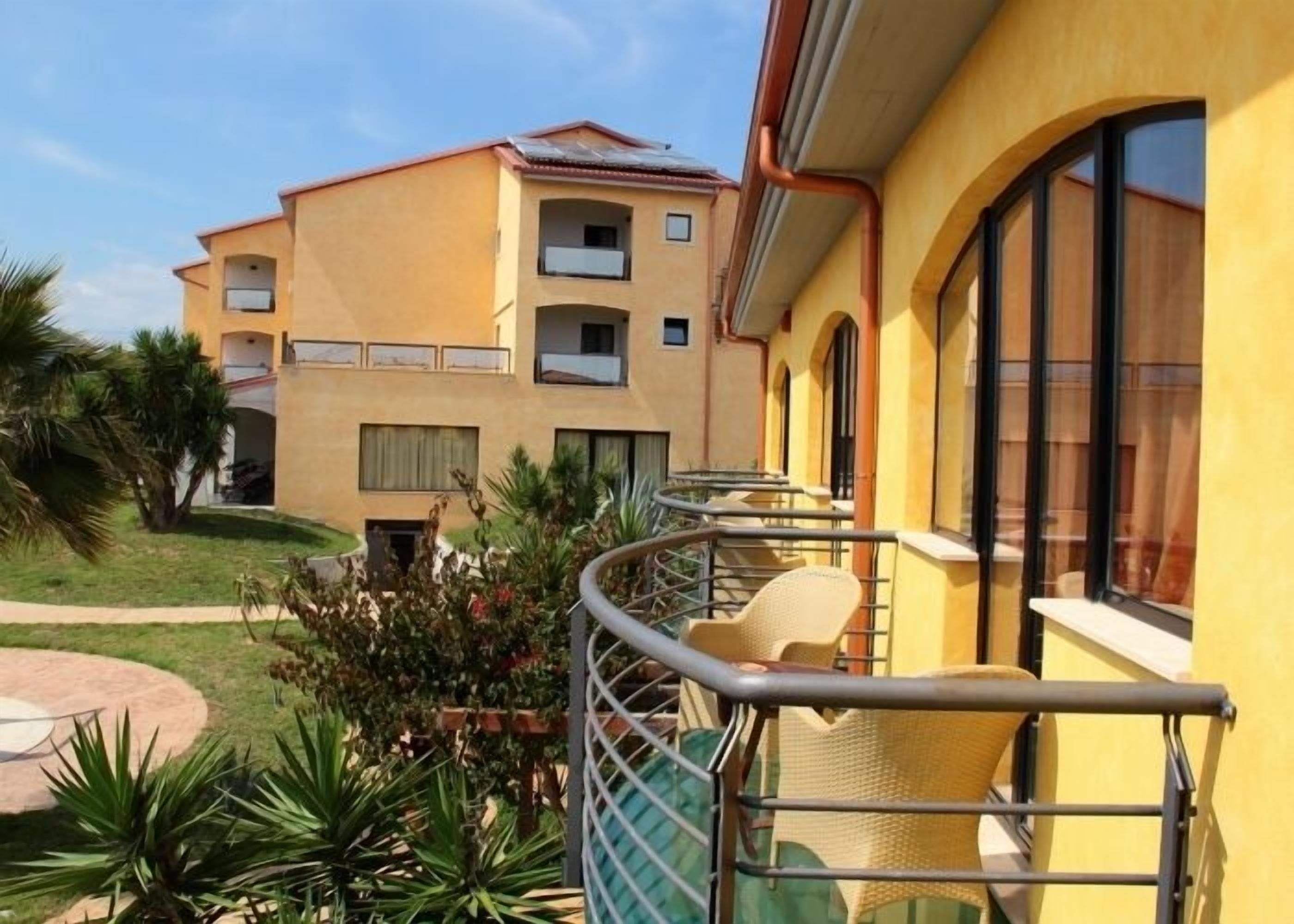 Ein gelbes Gebäude mit Balkon, umgeben von viel Grün und Palmen.
