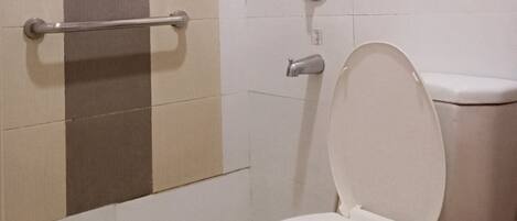 Un baño con inodoro, ducha y barra de apoyo.