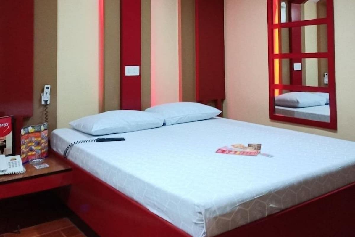 Une chambre avec un lit, une table de chevet, un miroir et une fenêtre à cadre rouge.