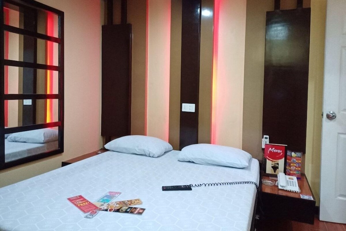 Une chambre d’hôtel avec un lit, une table de chevet, un miroir et une porte.