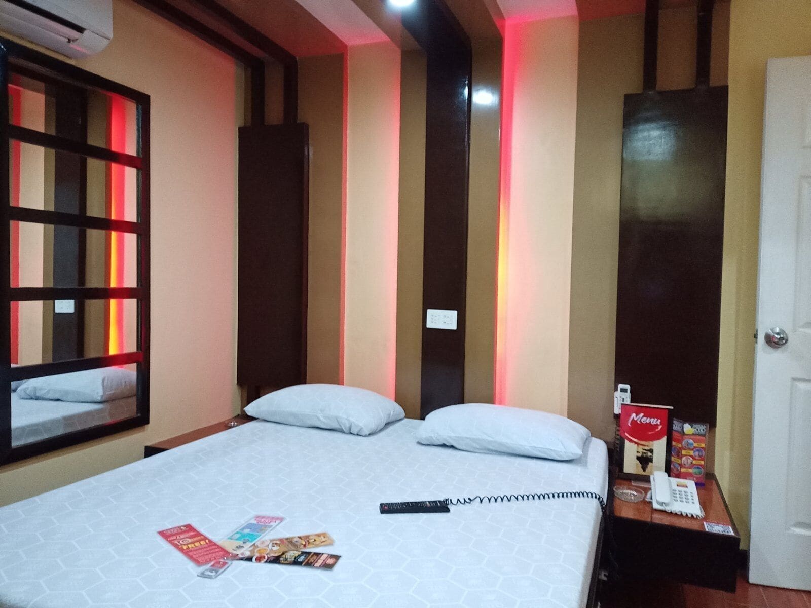 Ein Hotelzimmer mit einem Bett, einem Spiegel, einem Nachttisch mit Telefon und Speisekartenständer, sowie einer Wand mit vertikalen Streifen.