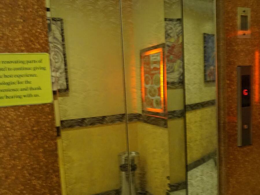 Un ascensore con porta in vetro, un cartello giallo sulla parete e una luce rossa sulla parete.