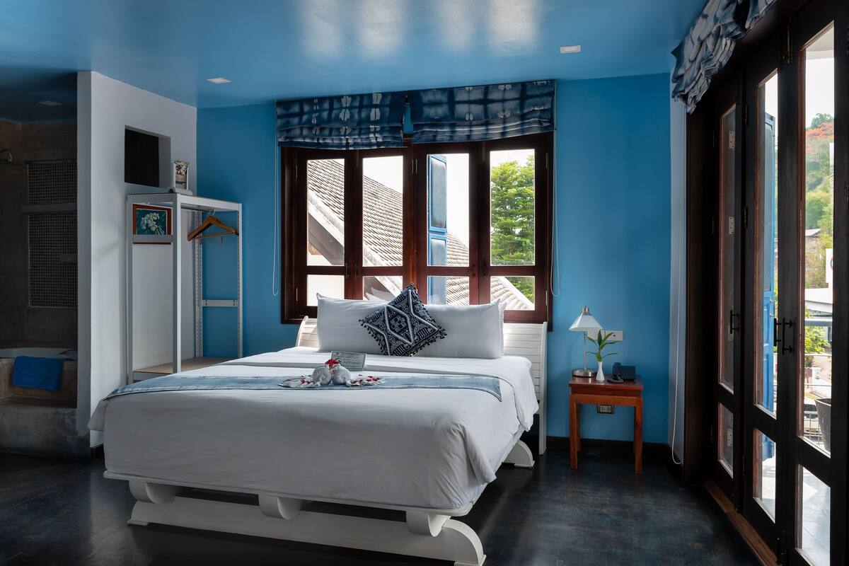 Un dormitorio con cama, mesita de noche, ventana con cortinas, armario y zona de ducha.