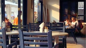 En restaurang med runda bord och blå stolar, stora fönster och utsikt över omgivningarna.
