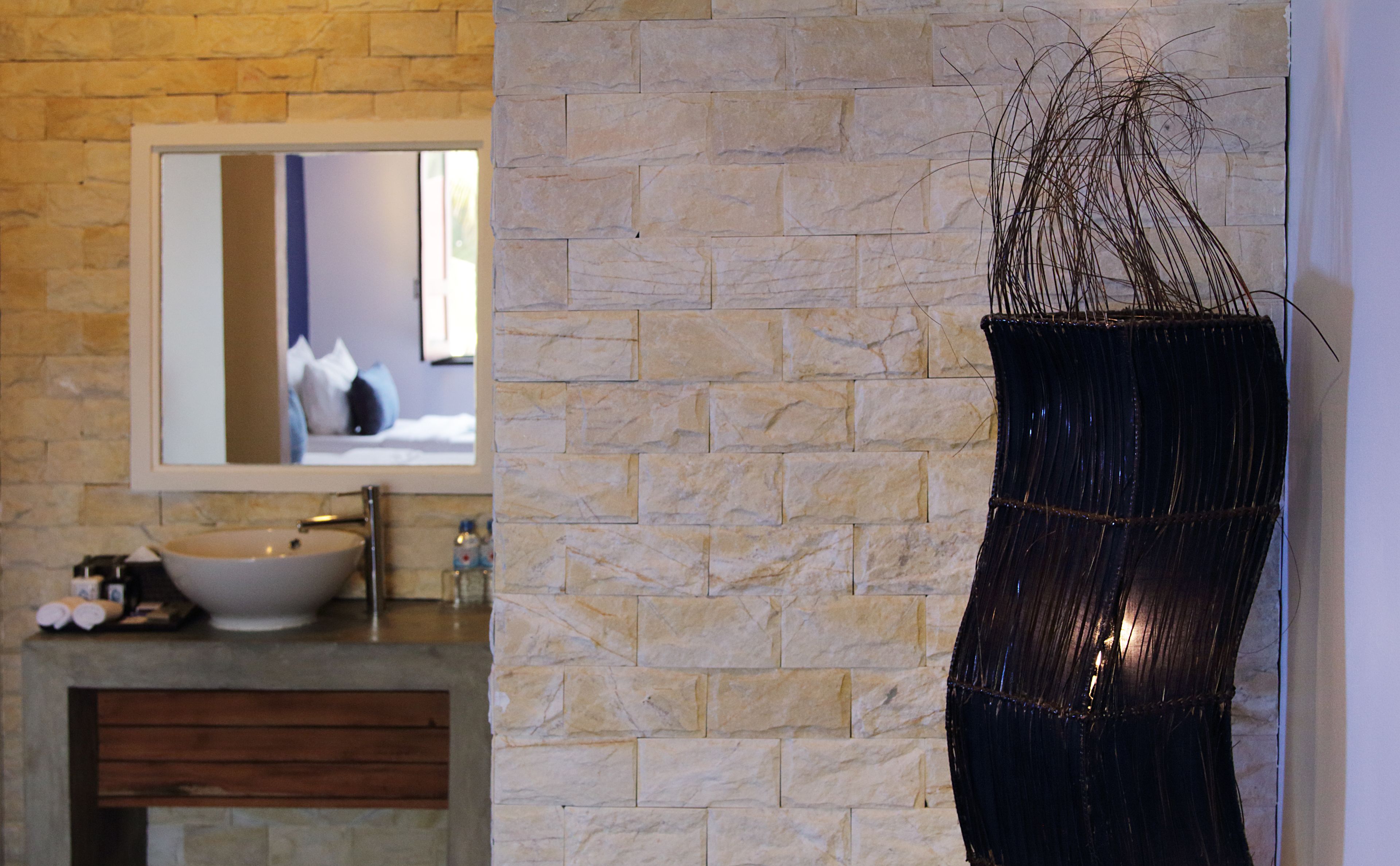 A bathroom with a stone wall, a white sink, and a mirror.