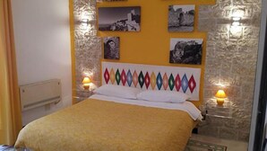 A bedroom with a bed, a stone wall, and artwork on the wall. - B&B Erice Antico Borgo (Erice)