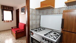 A compact kitchen with a gas stove, a refrigerator, and a red sofa. - B&B Erice Antico Borgo (Erice)