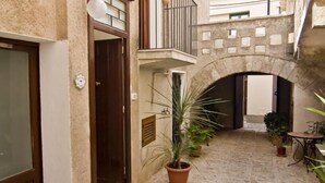 A narrow courtyard with a stone floor, a wooden door, and a potted plant. - B&B Erice Antico Borgo (Erice)