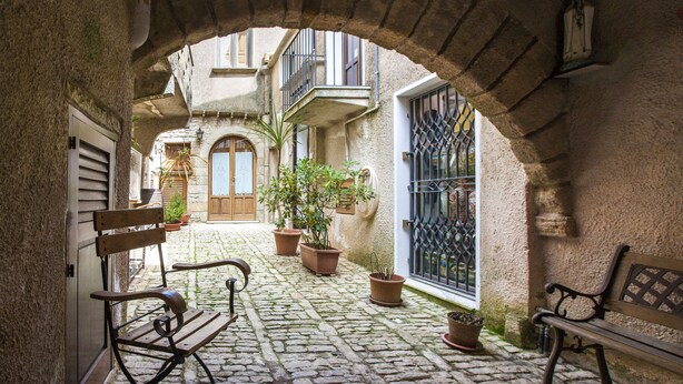 A cobblestone courtyard with benches, potted plants, and a wrought iron gate. - B&B Erice Antico Borgo (Erice)