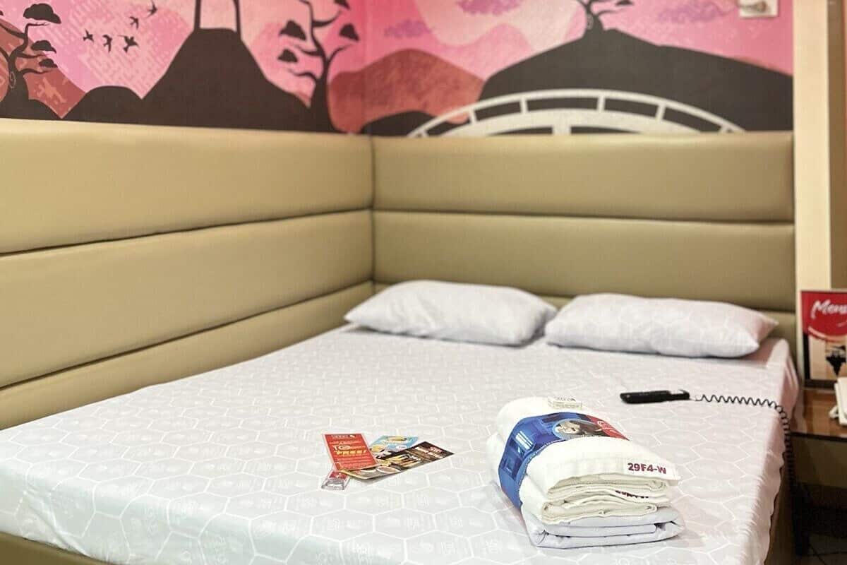 A hotel room with a bed, pillows, a magazine, and a folded towel.