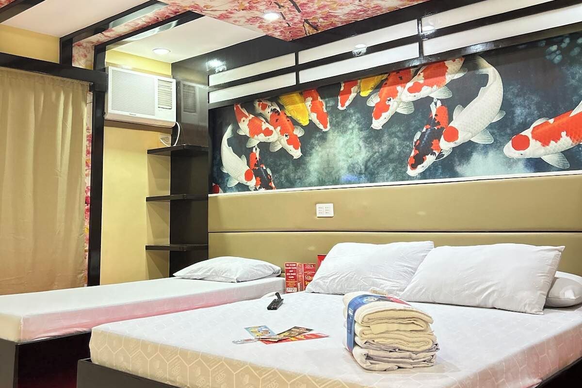 Una habitación de hotel con una cama, una mesita de noche, un aire acondicionado montado en la pared y un techo con motivos florales.