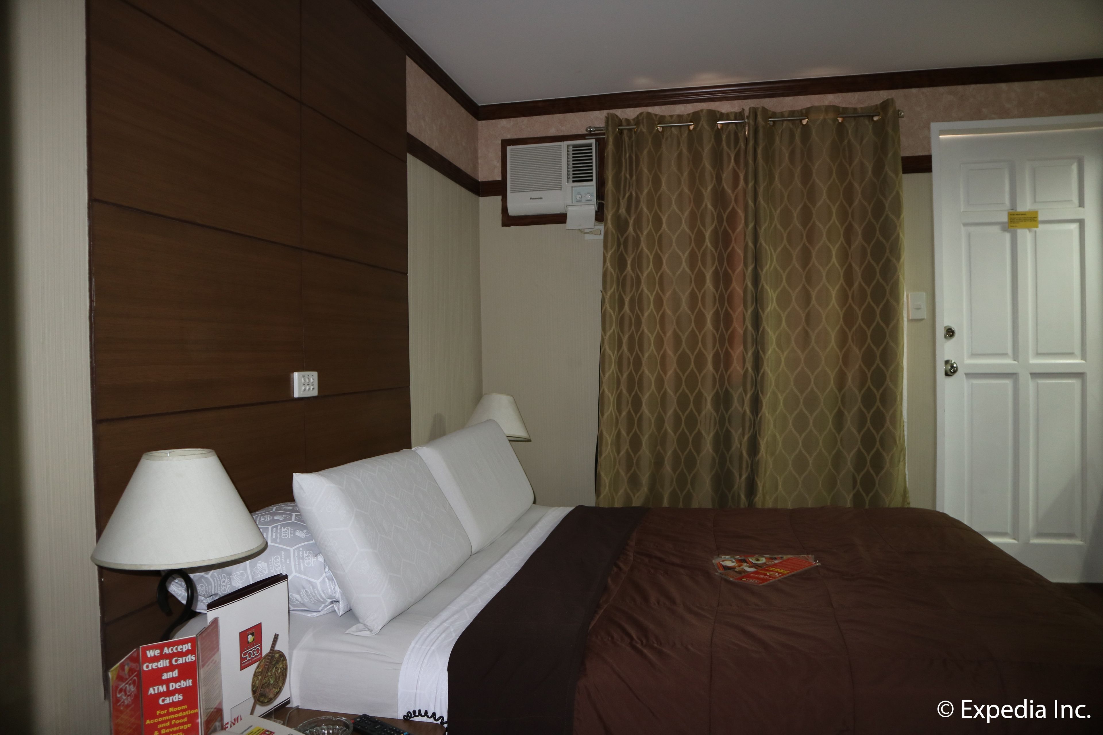 A hotel room with a bed, a lamp, a wall-mounted air conditioner, and a door with a lock.
