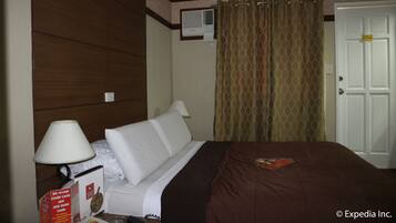 A hotel room with a bed, a lamp, a wall-mounted air conditioner, and a door with a lock.