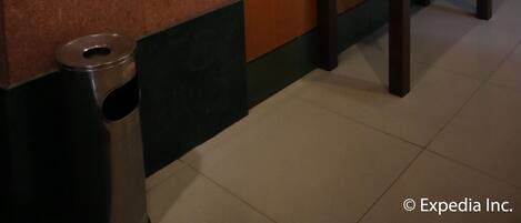 A lobby with a wooden panel wall, a mounted television, a digital elevator control panel, a framed artwork, and a small table with decorative items.