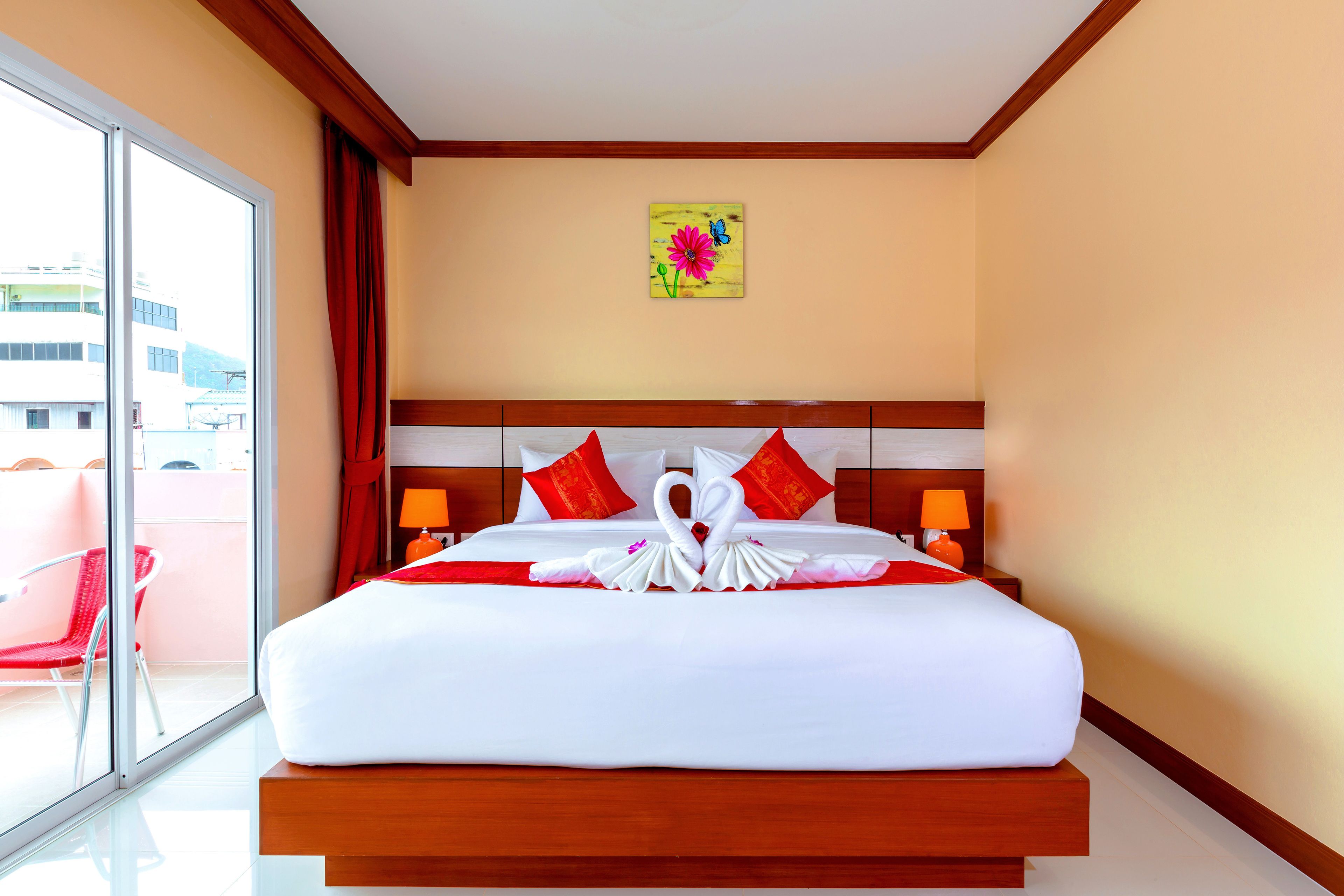 Een hotelkamer met een groot bed, rode kussens, een houten hoofdbord en een schilderij aan de muur.
