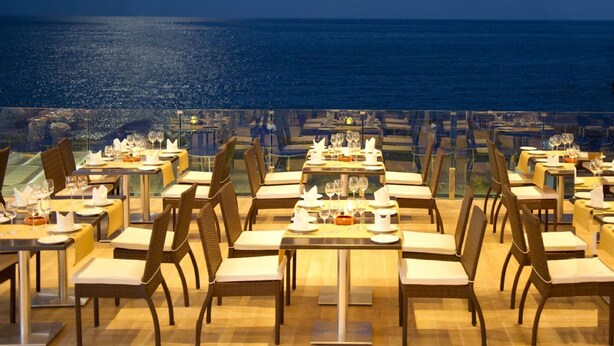 An outdoor dining area with tables set for two, overlooking a body of water. - Mare Blue Hotel (Ierapetra)