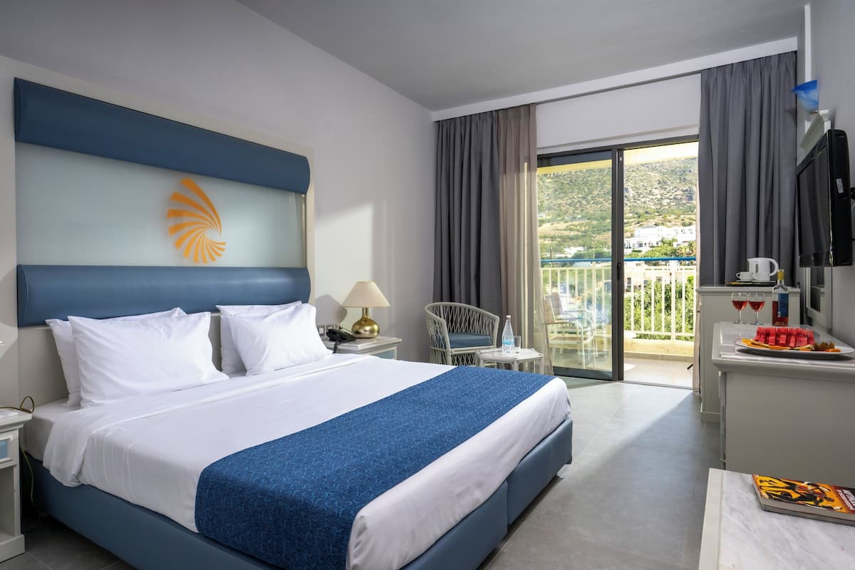 A hotel room with a bed, a desk, a chair, a TV, and a balcony with a view.