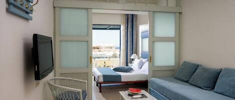 A hotel room with a bed, a sofa, a TV, a small table, and a balcony with a view.