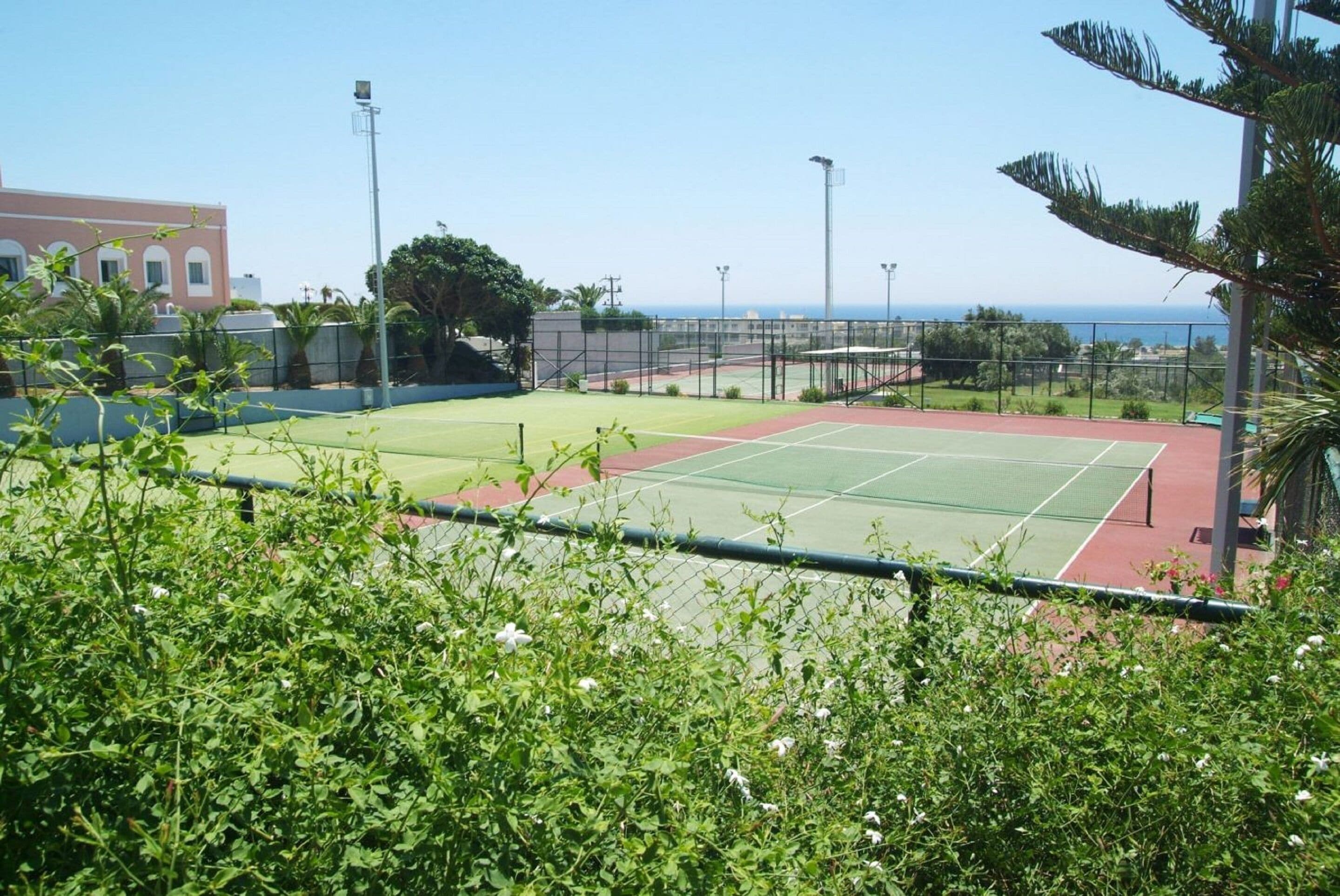 A tennis court with a net, surrounded by a fence, and a building in the background.