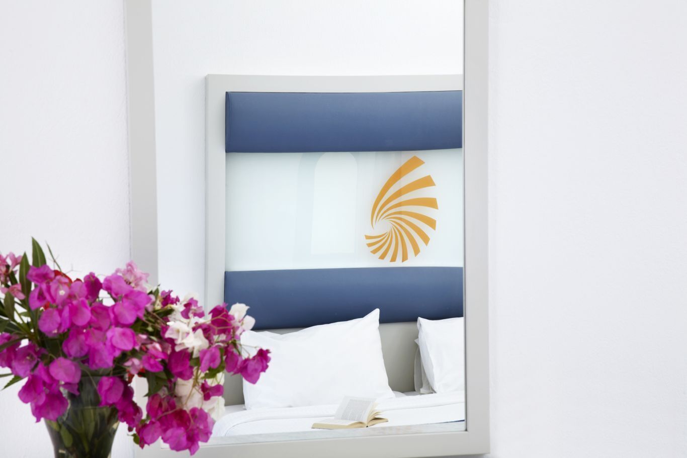 Une chambre d’hôtel avec un lit, des oreillers blancs, une tête de lit bleue et un logo orange décoratif sur le mur.
