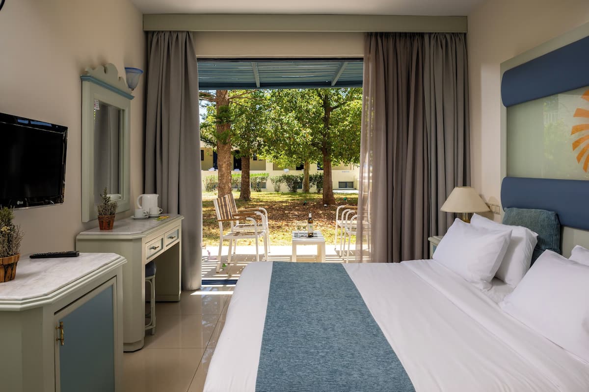 A hotel room with a bed, a desk, a TV, a window with curtains, and a view of the outdoors.