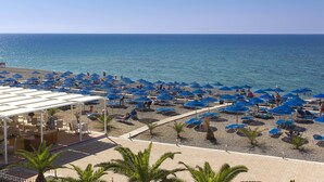 A beach with numerous blue umbrellas and sun loungers, a covered seating area, and a view of the sea. - Mare Blue Hotel (Ierapetra)