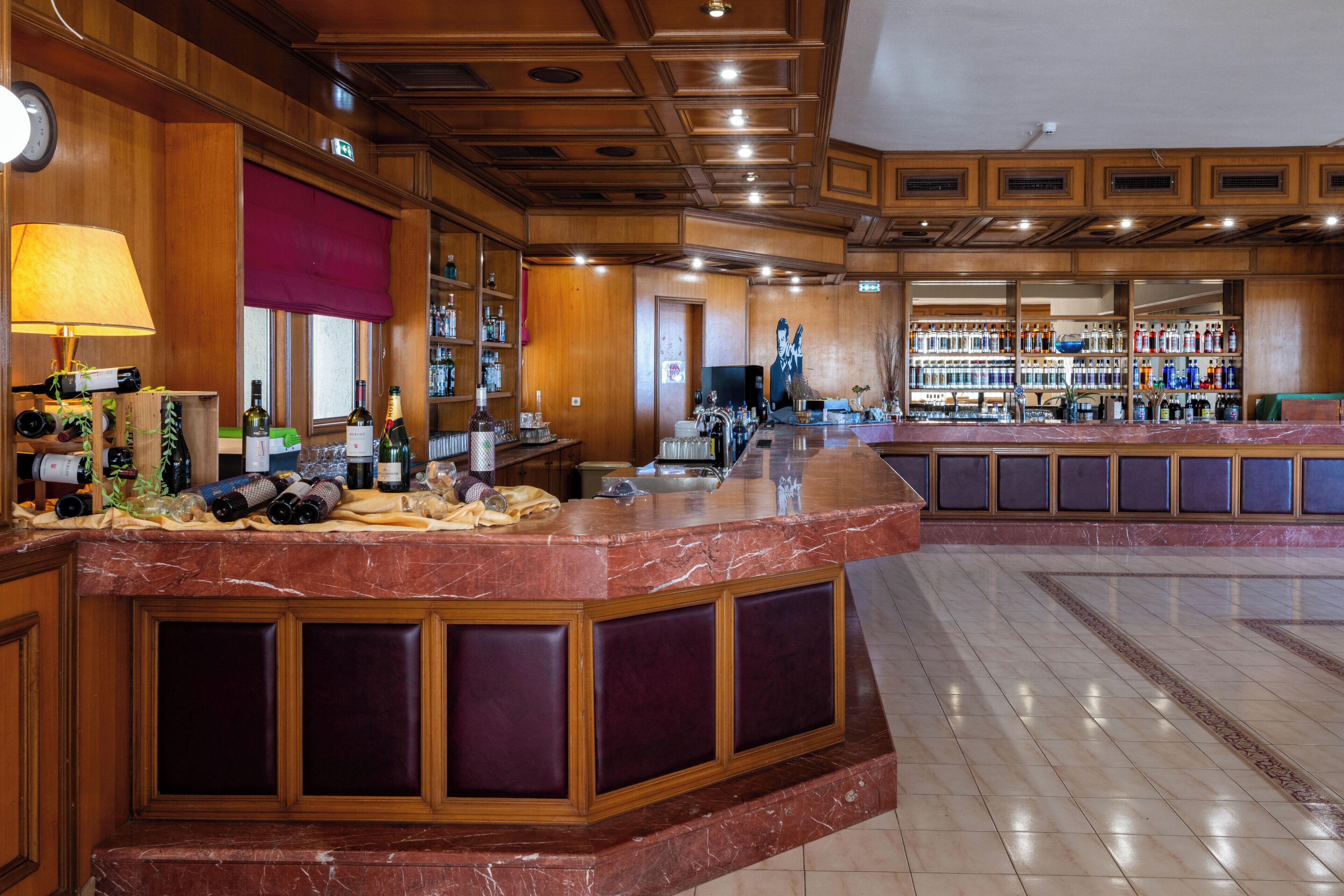 Una zona de bar con mostrador de mármol, paneles de madera y una variedad de botellas.