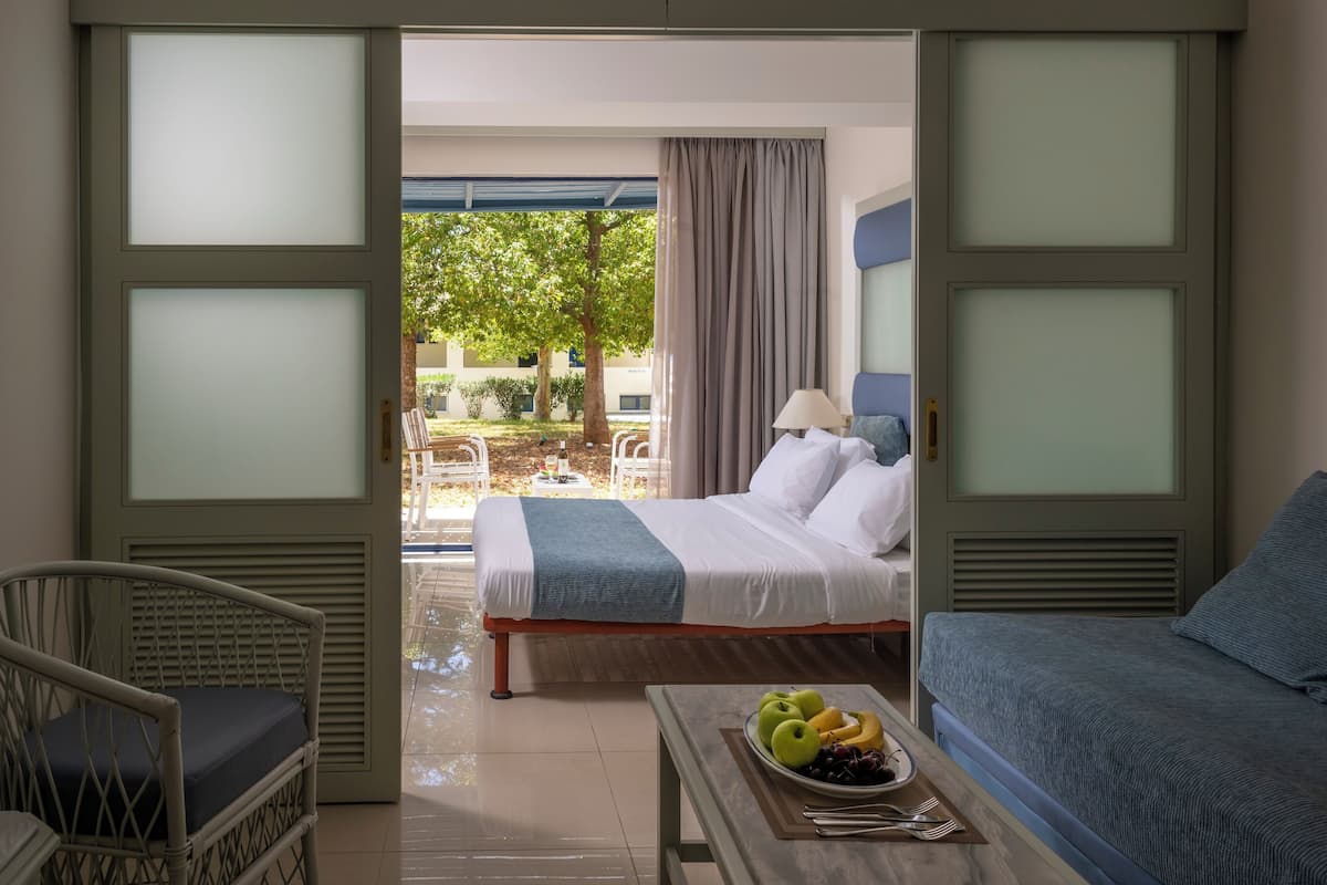 A hotel room with a bed, a chair, a table with fruit, and a view of the outdoors.