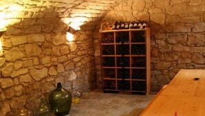 Une cave aux murs de pierre, avec une table et des bancs en bois, un meuble à bouteilles et deux bouteilles en verre vert.