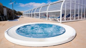 Un jacuzzi rodeado de sillones de descanso y una zona cerrada con vidrio y sillas.