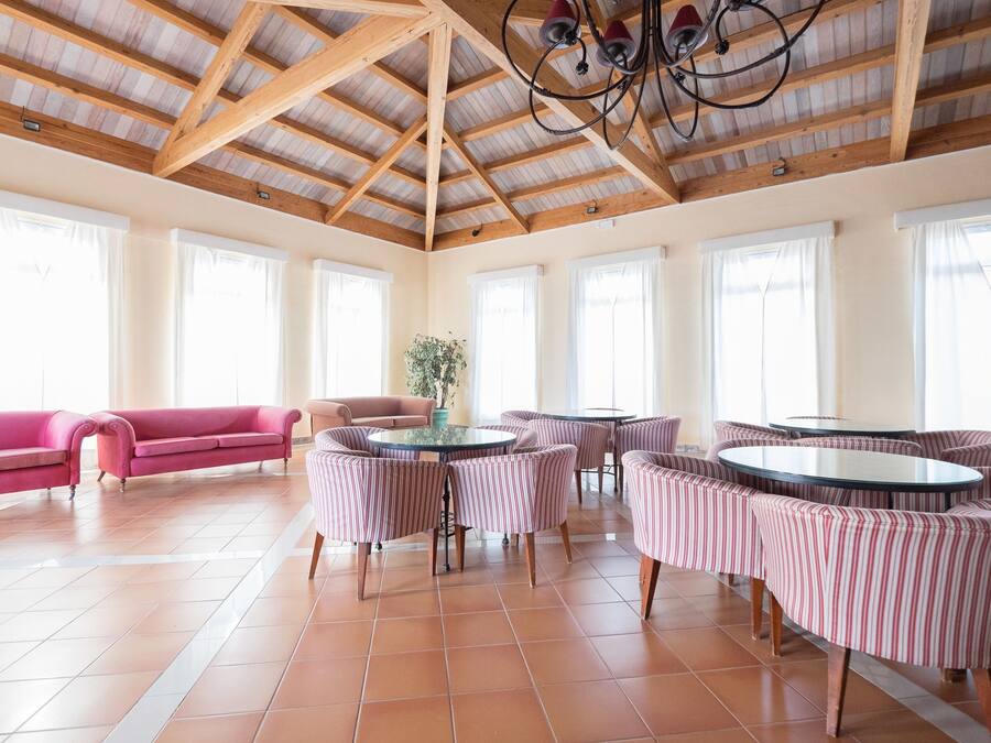 A spacious room with a high wooden ceiling, large windows, a pink sofa, striped armchairs, and a round table.