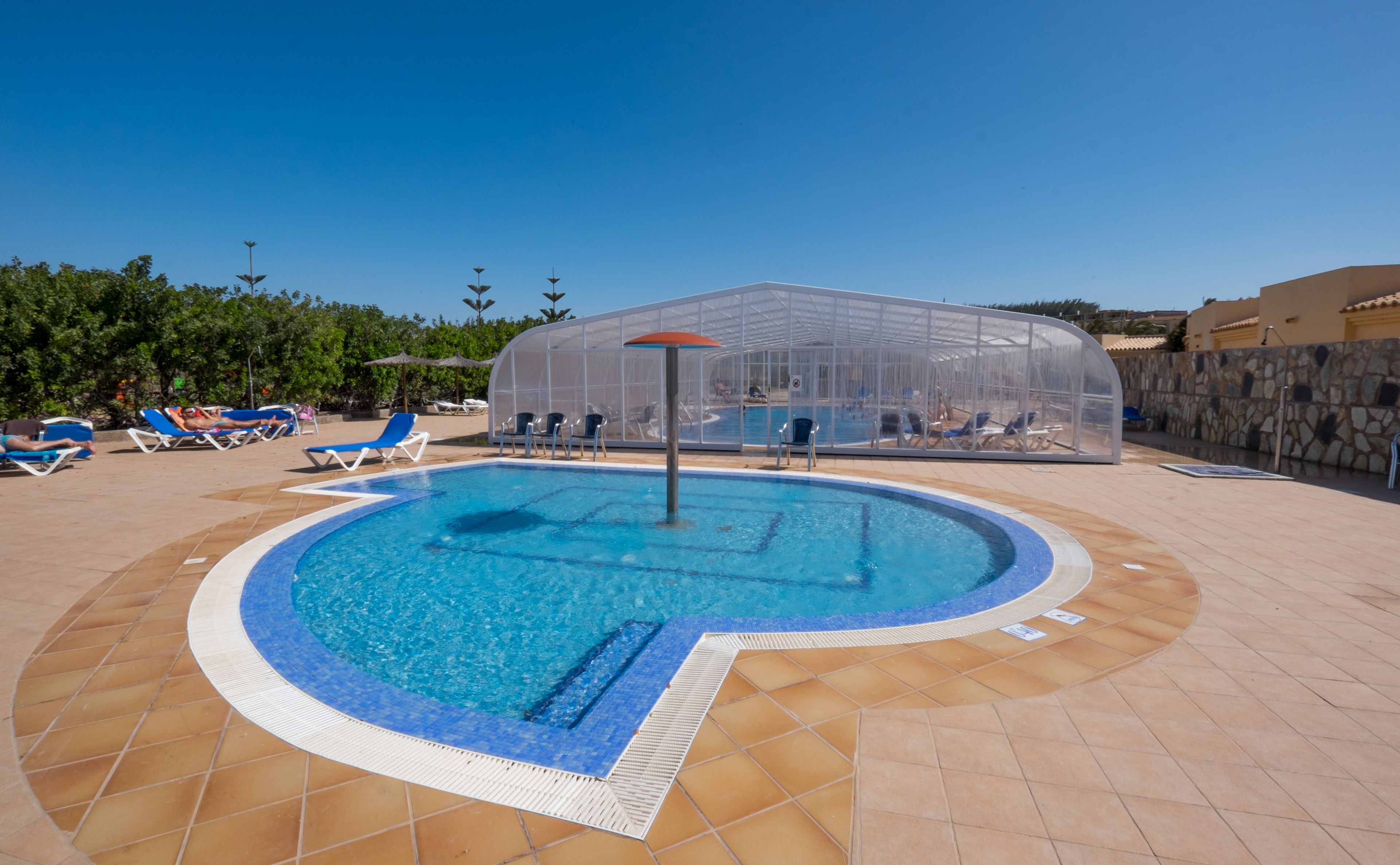Una piscina con solárium empedrado, rodeada de sillones de playa y sombrillas.