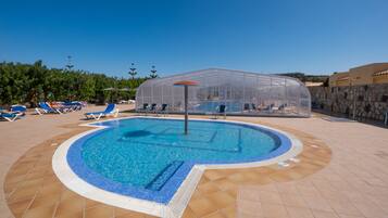Una piscina con solárium empedrado, rodeada de sillones de playa y sombrillas.