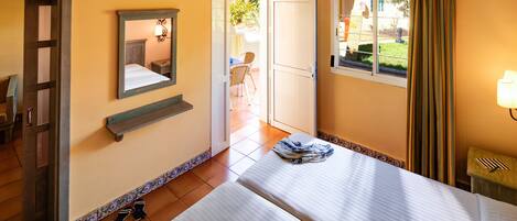 A hotel room with two beds, a ceiling fan, a window with curtains, and a small table with a lamp.