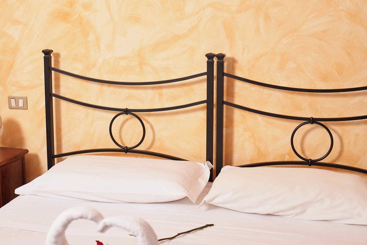 A bed with white linens, a rose, and two swan-shaped towels.
