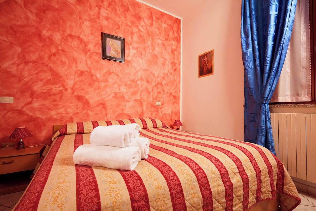 A hotel room with a bed, a nightstand, a lamp, and a window with curtains.